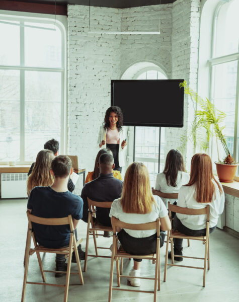 Female african-american speaker giving presentation in hall at workshop. Audience or conference hall. Rear view of participants in audience. Conference event, training. Education, diversity, inclusive concept.