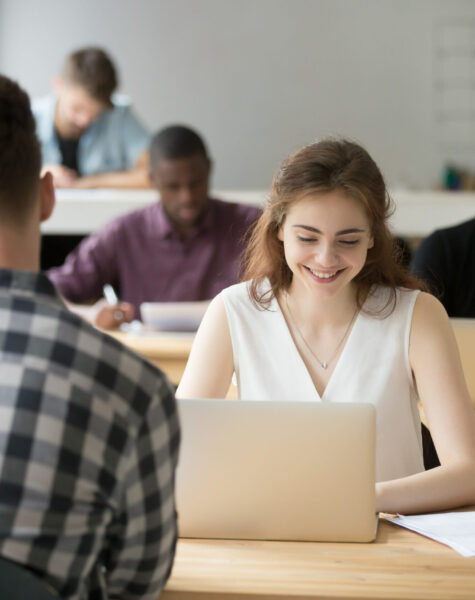 Young smiling woman working on laptop in coworking office, happy employee using computer sitting at desk in team shared space, attractive female student or client sales manager using pc at workplace